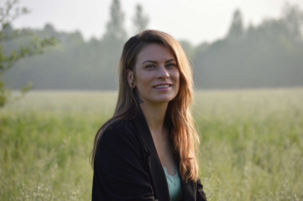 Vriendelijke, lachende vrouw in een natuurlijke, mistige grasweide met een zwarte blazer.